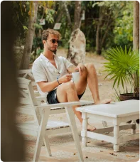 Homem sentado em ambiente de férias entre vegetação verde com palmeiras